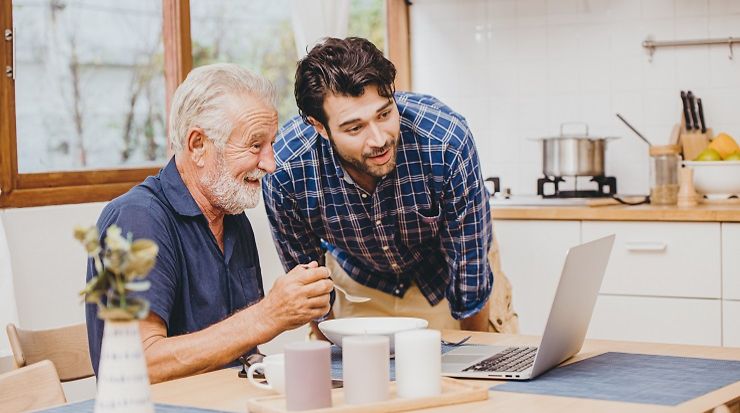 Young man looks at laptop with happy older man, who is operating the laptop