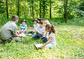 Kinder sitzen mit einem Erwachsenen im Wald und lernen aus Büchern